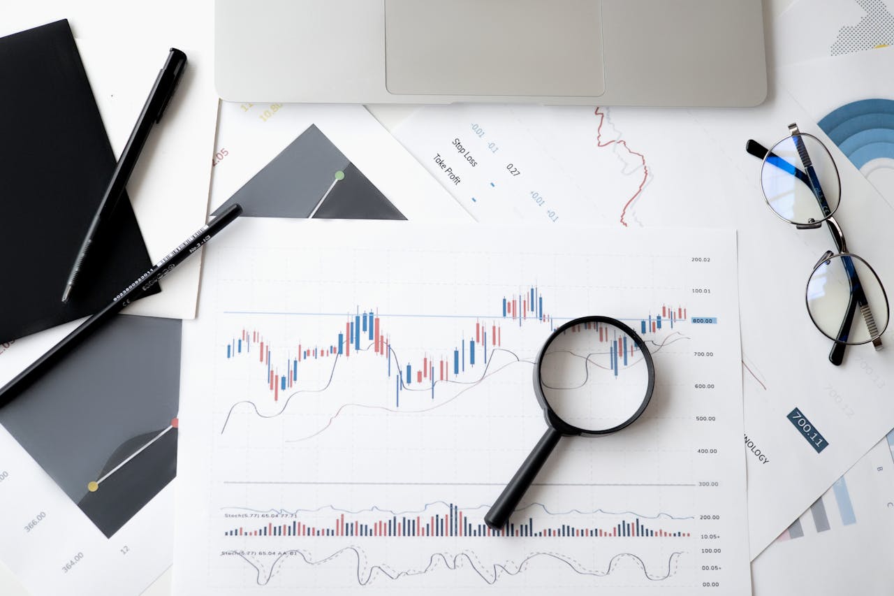 cta-bg Flat lay of stock market analysis documents with magnifying glass, pens, and glasses.