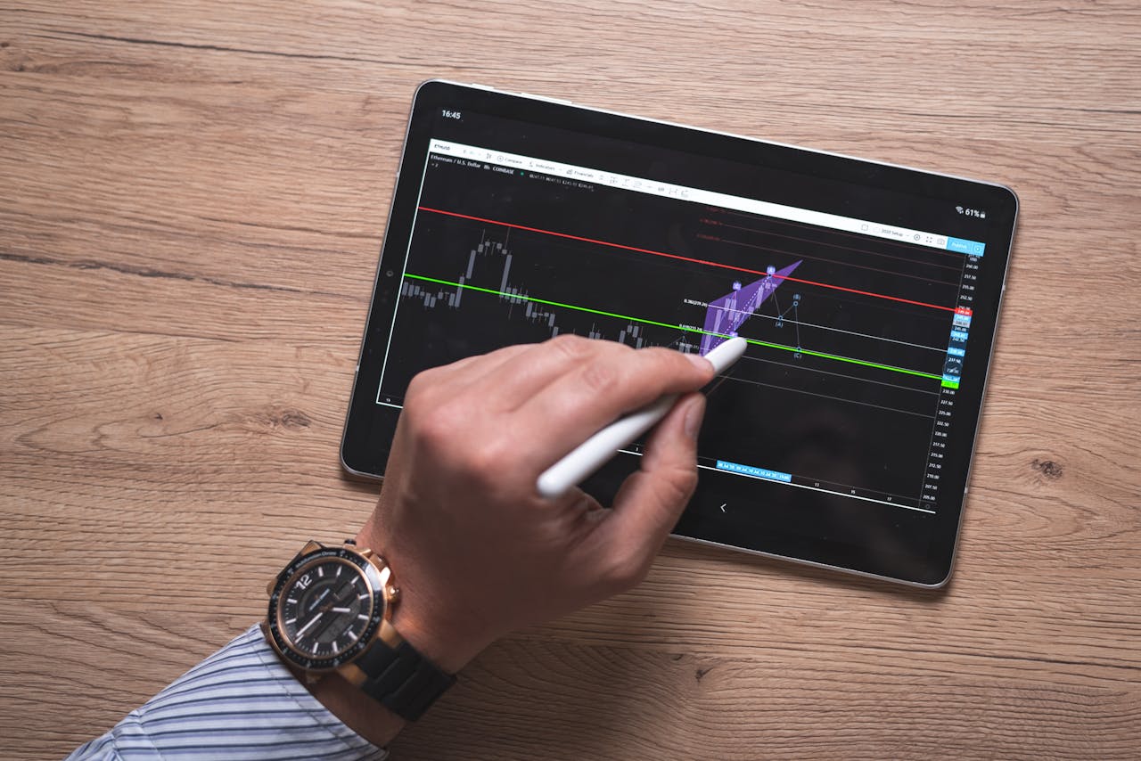 testimonials-img Close-up of a hand using a stylus on a digital trading app on a tablet indoors.