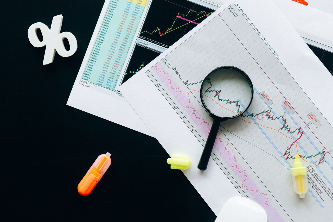 home-hero-bg High-angle view of financial charts, showcasing stock market analysis with magnifying glass and highlighters.
